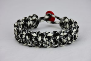 black and white camouflage paracord bracelet with red button, picture of a black and white camouflage paracord bracelet with red button fastener in the back on a white background
