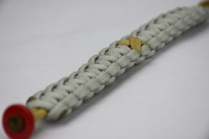 gold and grey pediatric cancer support paracord bracelet with gold ribbon and red button in the front corner