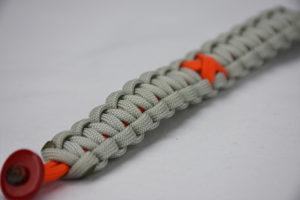 orange and grey leukemia support paracord bracelet with red button fastener in the corner of the image and orange support ribbon in the center