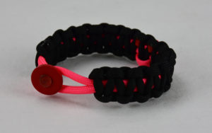 pink and black breast cancer support paracord bracelet with red button fastener in the front and pink ribbon