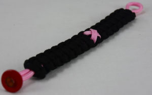soft pink and black breast cancer support paracord bracelet with red button in the bottom corner and a soft pink ribbon