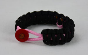 soft pink and black breast cancer support paracord bracelet with red button fastener in the front and a soft pink ribbon