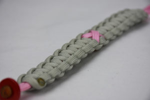 soft pink and grey breast cancer support paracord bracelet, picture of a soft pink and grey breast cancer support paracord bracelet unity band with a pink ribbon in the center and red button fastener in the corner