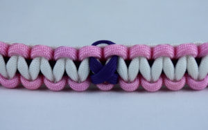 black soft pink and white alzheimers support paracord bracelet with purple ribbon in the center of a white background