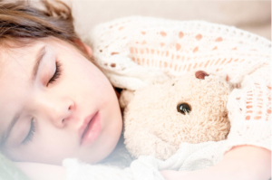 picture of a kid sleeping peacefully with a teddy bear in her arms.