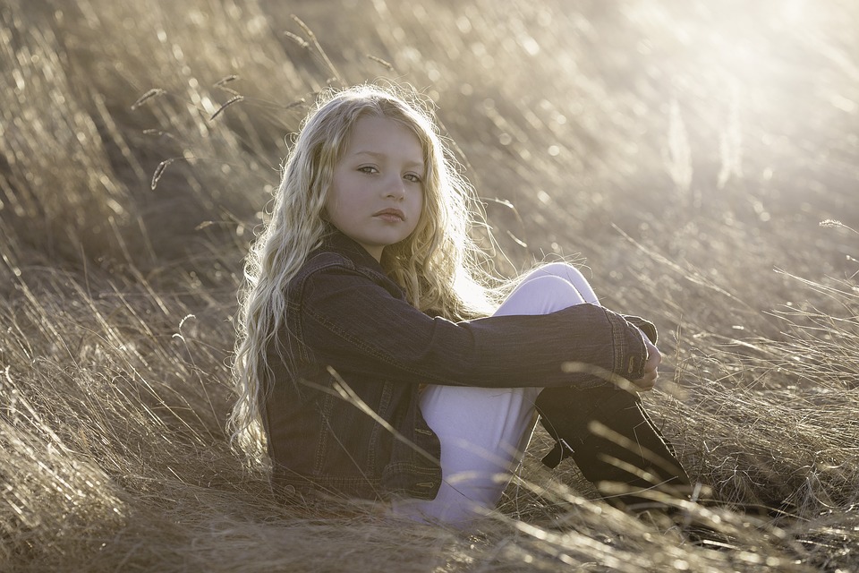 young kid sitting in a field looking somber